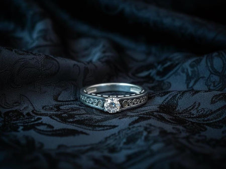 A detailed macro shot of a sterling silver engagement ring. The focal point is a round, honey-colored gemstone (Citrine or Madeira Topaz) set flush into the band. The shank is decorated with a continuous relief pattern of spirals and circles, mimicking the decorative robes found in Gustav Klimt's "Golden Phase" paintings. The silver features an oxidized finish, creating a dark background that makes the polished spirals pop.