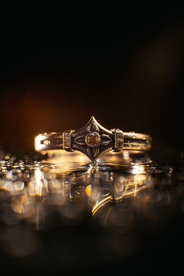 A high-resolution macro photograph of a matching sterling silver gothic wedding ring set resting on softly draped, luxurious white satin. The set features a wider masculine band and a slightly narrower feminine band. Both rings display a continuous engraved arcade of pointed medieval arches along the bottom edge, centering on a polished geometric rhombus frame that holds a brilliant round white gemstone. The polished silver beautifully contrasts  (etsy image id: 7928017042)