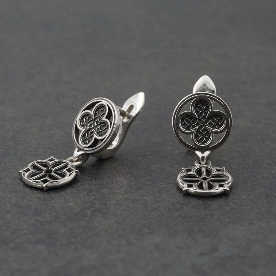 The image highlights the specific textures of the casting. The top stud has a "waffle" or lattice texture inside the quatrefoil lobes, mimicking chainmail or stone carving. The bottom drop is smooth and open, providing a visual counterweight. The 925 sterling silver is treated with an antique patina to enhance the "old world" feel. Modeled as a versatile daily earring, the "coin" size is modest enough for office wear (etsy image id: 5775868859)