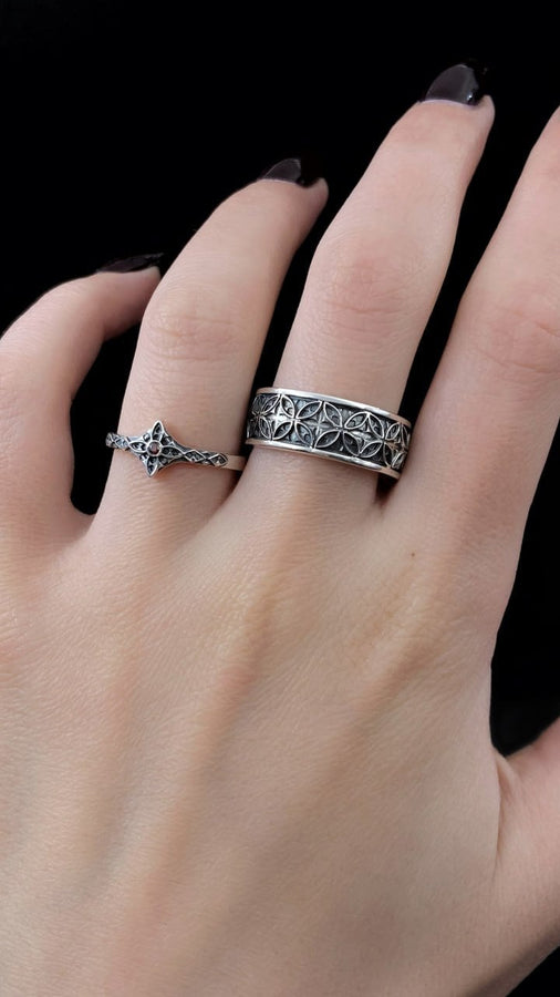 A professional studio photograph of a matching two-piece sterling silver wedding ring set. Both rings feature a prominent, raised Greek-style cross motif in the center, which holds a round, bezel-set white crystal. The interior of the cross arms has a fine, cross-hatched grid texture. Along the sides of the high-polished silver bands are recessed, four-lobed quatrefoil shapes. The rings are presented against a pitch-black background, making the p __etsy:8051335185