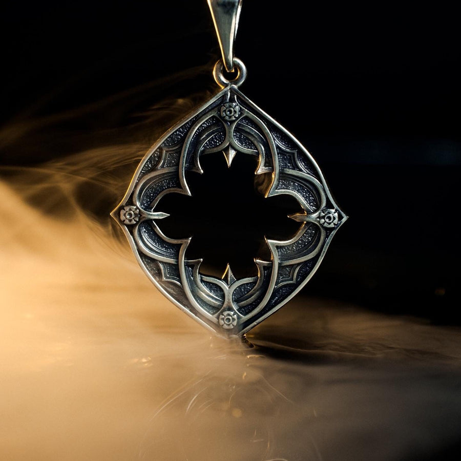 Sterling Silver Gothic Pendant, Holiday Gift, Handmade Medieval Pendant, Goth Necklace, Gothic Jewelry, A cinematic studio shot of a diamond-shaped sterling silver pendant hanging against a smoky, amber-lit background. The design is "openwork," featuring a central cutout in the shape of a four-lobed quatrefoil with sharp, barbed cusps. The silver frame mimics the stone mullions of a Gothic window. The metal is polished on the ridges and (etsy image id: 6258009905)