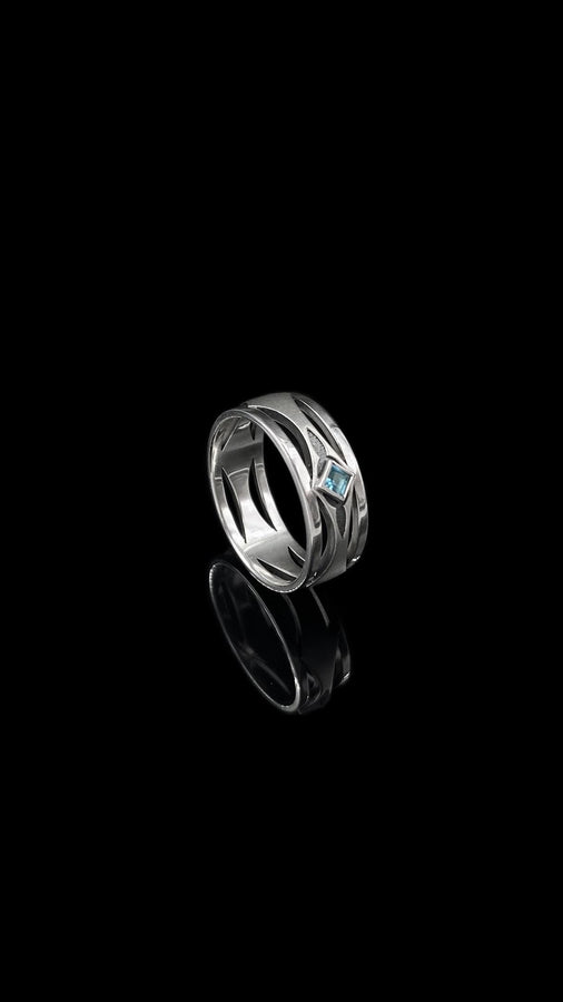 This Art Deco wedding ring set features a sterling silver engagement ring and matching band with bold geometric cutouts and a bright blue square gemstone. The clean lines, layered shapes, and sculptural silhouette create a modern yet vintage feel ideal for couples seeking unique, architecturally inspired bridal jewelry captured on a reflective surface for elegant presentation.