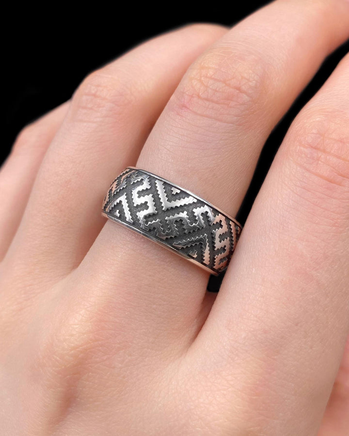 A studio shot of a two-piece sterling silver ring set with a high-contrast black and silver finish. The standing ring features a square, diamond-shaped face created by stepped geometric lines. The lying ring is a wide band with a continuous "zig-zag" or "step" pattern running around the circumference. The design mimics the look of cross-stitch embroidery or pixelated ancient art rendered in metal.