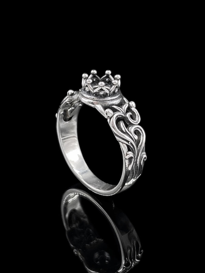 A high-contrast studio shot of a two-piece sterling silver ring set. The top ring features a raised, three-dimensional "crown" or "coronet" motif with small spheres on the tips. The bottom ring is a matching wide band. Both rings are covered in intricate, raised scrollwork or vine-like filigree. The silver is polished bright on the raised swirls, contrasting with the black oxidized background.