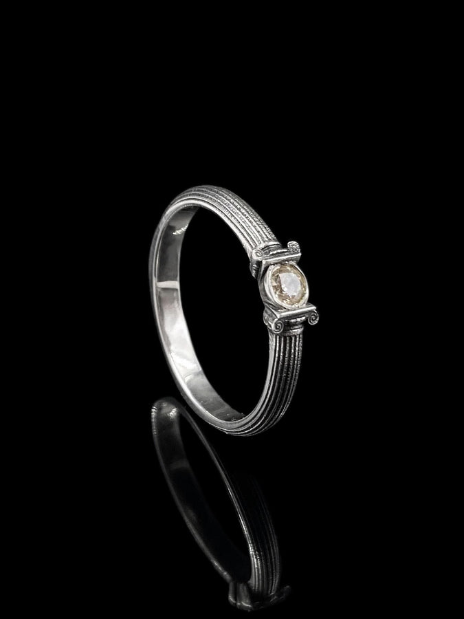 The photograph captures a slim Victorian silver ring with a gemstone framed by sculpted column motifs. Fine linear textures cover the band, giving it a classical, antique appeal. The gemstone sparkles softly, contrasting the darker oxidized grooves. This intricate design suits those who appreciate architectural jewelry, artistic detailing, and meaningful handmade engagement pieces. (etsy image id: 6976743880)