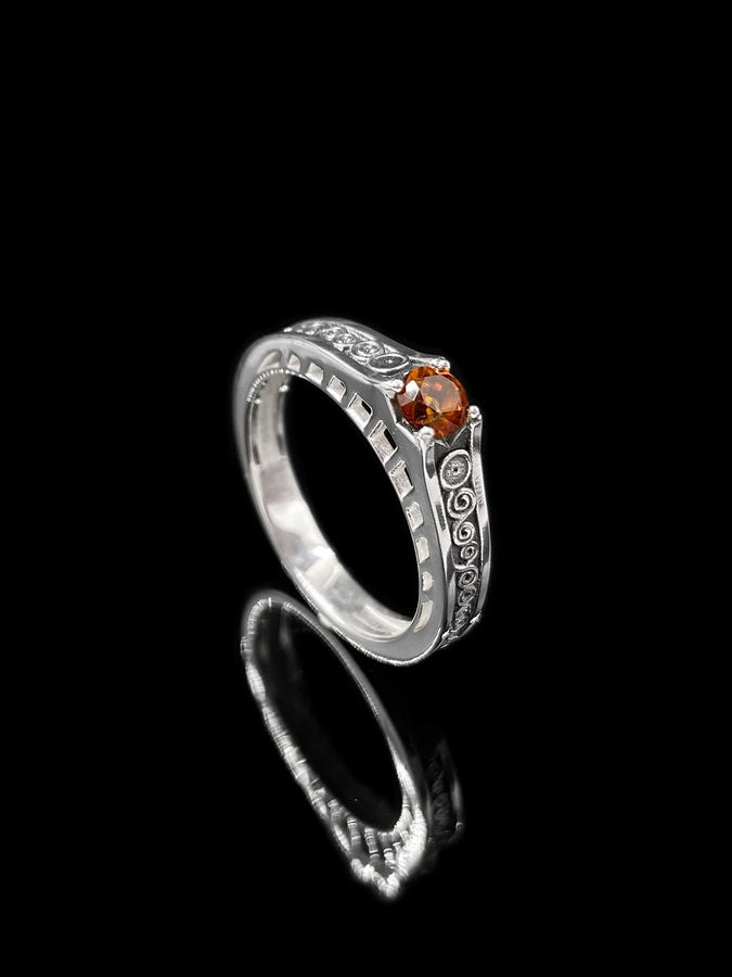 A cinematic studio shot of a matching two-piece ring set. The bottom ring is a wide silver band featuring a detailed relief carving of the couple from Gustav Klimt's "The Kiss." The top ring is a narrower engagement band that mimics the geometric patterns of the painting and holds a round, amber-colored gemstone. The background is a warm, golden haze, reflecting the "Golden Phase" of the original artwork.