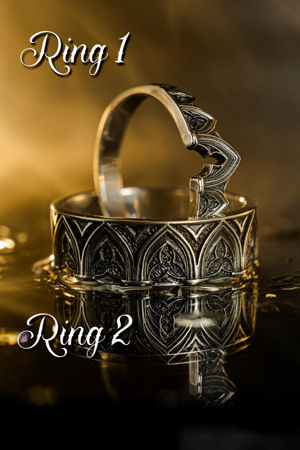 A cinematic studio shot of two matching sterling silver rings. The top ring is a delicate "crown" or tiara shape, formed by the peak of a Gothic arch with trefoil tracery. The bottom ring is a wide band featuring a continuous row of identical arches. The background metal inside the arches has a rough, "eroded" or stippled texture, heavily oxidized to black, while the raised architectural lines are polished smooth.