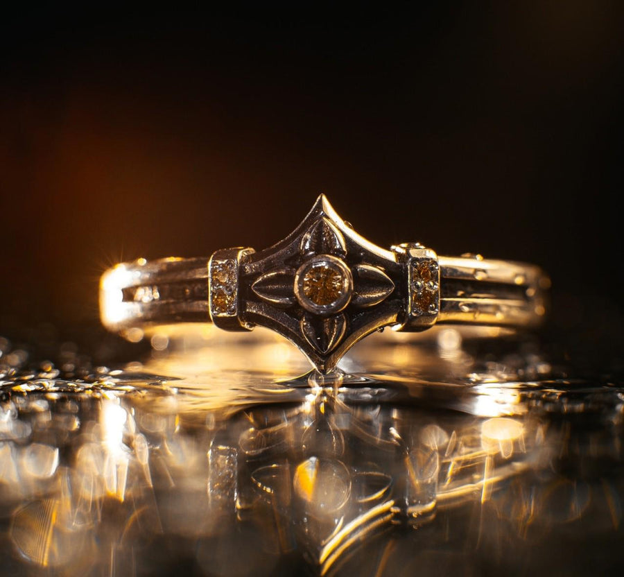 A high-resolution macro photograph of a matching sterling silver gothic wedding ring set resting on softly draped, luxurious white satin. The set features a wider masculine band and a slightly narrower feminine band. Both rings display a continuous engraved arcade of pointed medieval arches along the bottom edge, centering on a polished geometric rhombus frame that holds a brilliant round white gemstone. The polished silver beautifully contrasts  (etsy image id: 7928017042)
