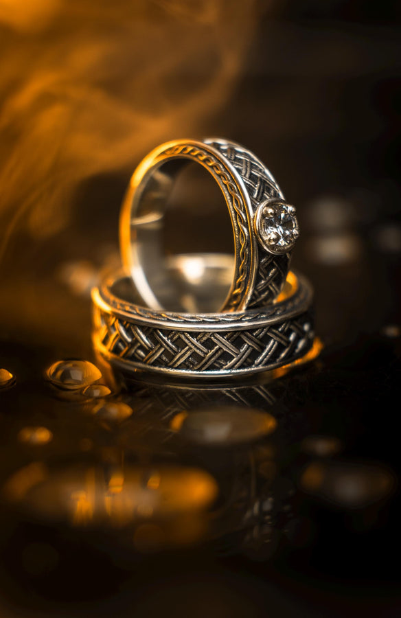 A cinematic studio shot of a wide sterling silver ring lying on a reflective golden surface. The band features a central "basket weave" pattern—diagonal strands of silver crossing over and under each other. The edges are framed by a distinct "rope" or "cable" twist border. The raised metal is polished silver, while the deep recesses are blackened to highlight the intricate weaving.