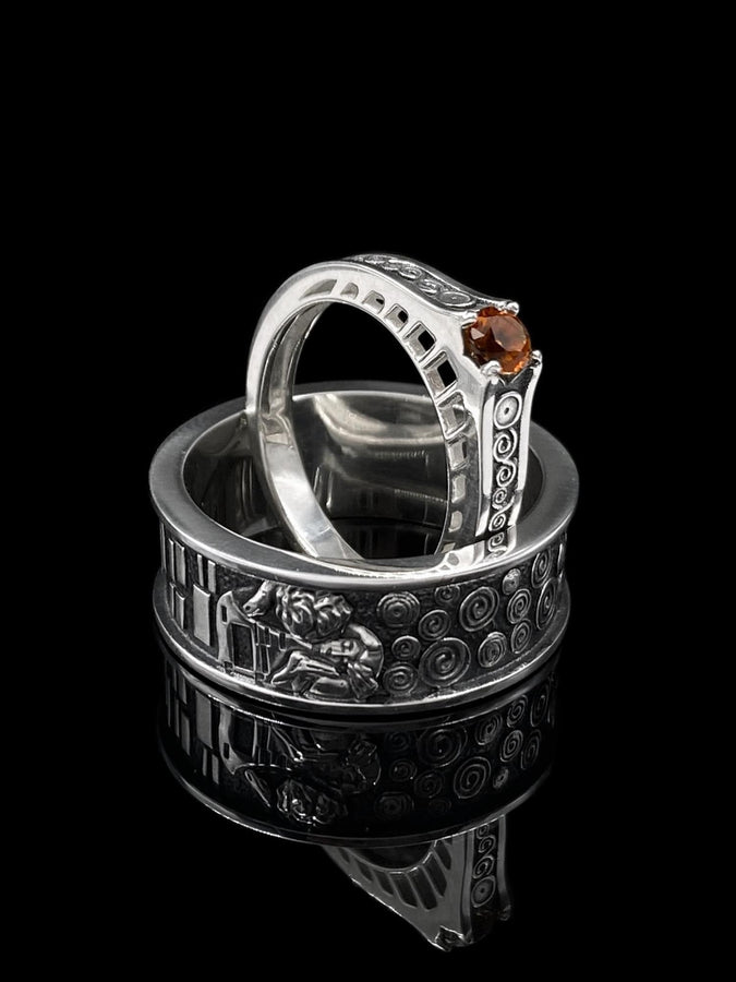 A detailed macro shot of a sterling silver engagement ring. The focal point is a round, honey-colored gemstone (Citrine or Madeira Topaz) set flush into the band. The shank is decorated with a continuous relief pattern of spirals and circles, mimicking the decorative robes found in Gustav Klimt's "Golden Phase" paintings. The silver features an oxidized finish, creating a dark background that makes the polished spirals pop. (etsy image id: 7142785932)
