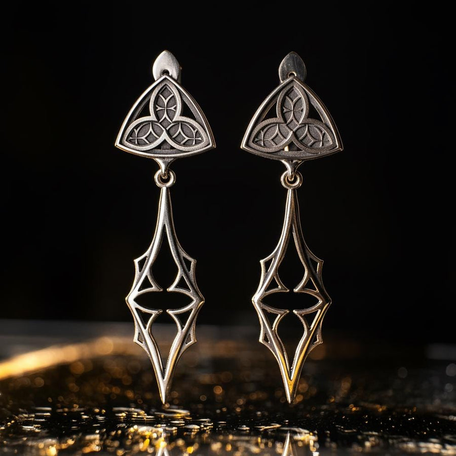 Embrace your dark beauty with our Gothic silver earrings. Unique design, premium silver, intricate details, and comfortable to wear.
A sharp studio shot of a pair of articulated silver earrings. The top stud is a soft triangle shape containing a raised "trefoil" or "trinity" knot pattern against a textured background. The bottom section is an elongated, openwork drop that tapers to a sharp point, resembling a Gothic spire or a (etsy image id: 7218877462)