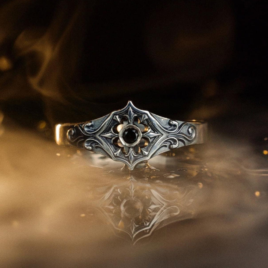 Close-up view of a gothic floral silver ring showcasing a detailed rose-inspired pattern and a polished black gemstone set in the middle. The intricate scrollwork surrounding the stone resembles cathedral tracery, giving the ring an old-world, medieval look. Perfect for engagement, weddings, anniversaries, or collectors of dark romantic jewelry and handcrafted artistic pieces. (etsy image id: 7243100328)