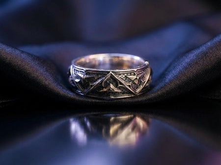 A close-up of a handcrafted sterling silver ring featuring a repeating pattern of Gothic pointed arches. The raised metal lines are highly polished, gleaming against a textured, matte black background created through heavy oxidation. The intricate relief mimics the stone tracery found in medieval cathedral windows, offering a rugged yet sophisticated appearance. The ring sits on a reflective black surface, highlighting the depth of the carving an (etsy image id: 7430797062)