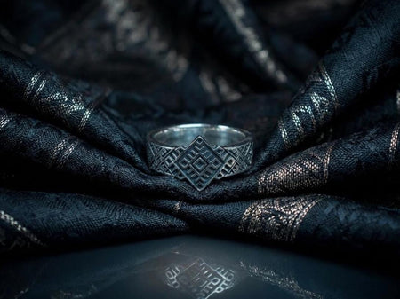A centered studio shot of a wide sterling silver ring. The focal point is a large, diamond-shaped geometric motif with stepped edges, resembling a pixelated sun or star. The sides of the band feature a finer "cross-stitch" lattice pattern. The raised design is polished silver, contrasting sharply with the matte black oxidized recesses, giving the metal a graphic, high-visibility appearance. (etsy image id: 7438600296)