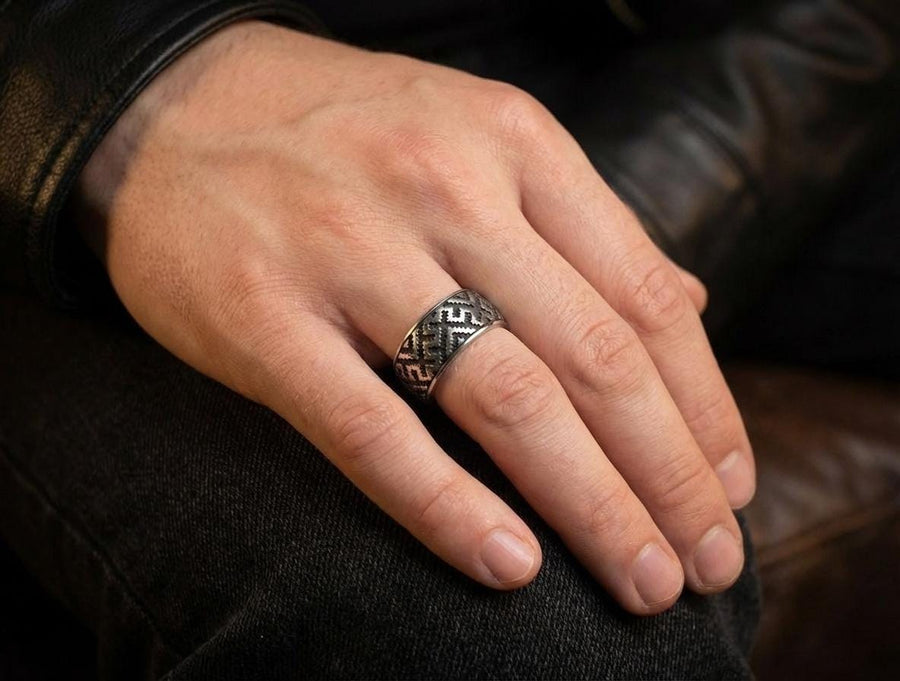 A studio shot of a two-piece sterling silver ring set with a high-contrast black and silver finish. The standing ring features a square, diamond-shaped face created by stepped geometric lines. The lying ring is a wide band with a continuous "zig-zag" or "step" pattern running around the circumference. The design mimics the look of cross-stitch embroidery or pixelated ancient art rendered in metal.