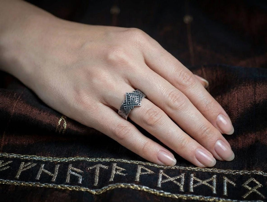 A studio shot of a two-piece sterling silver ring set with a high-contrast black and silver finish. The standing ring features a square, diamond-shaped face created by stepped geometric lines. The lying ring is a wide band with a continuous "zig-zag" or "step" pattern running around the circumference. The design mimics the look of cross-stitch embroidery or pixelated ancient art rendered in metal.