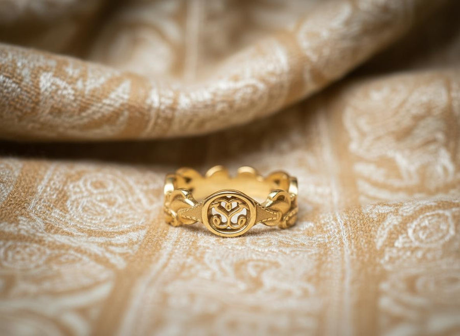 A cinematic macro shot of a sterling silver ring bathed in warm, golden light. The focal point is the central oval face, which encloses a raised relief design of two spirals meeting in the center to suggest a heart shape. The band shoulders feature textured knotwork that leads up to the centerpiece. The ring rests on a wet, reflective surface, creating a mirror image of the love knot below. (etsy image id: 7490345549)