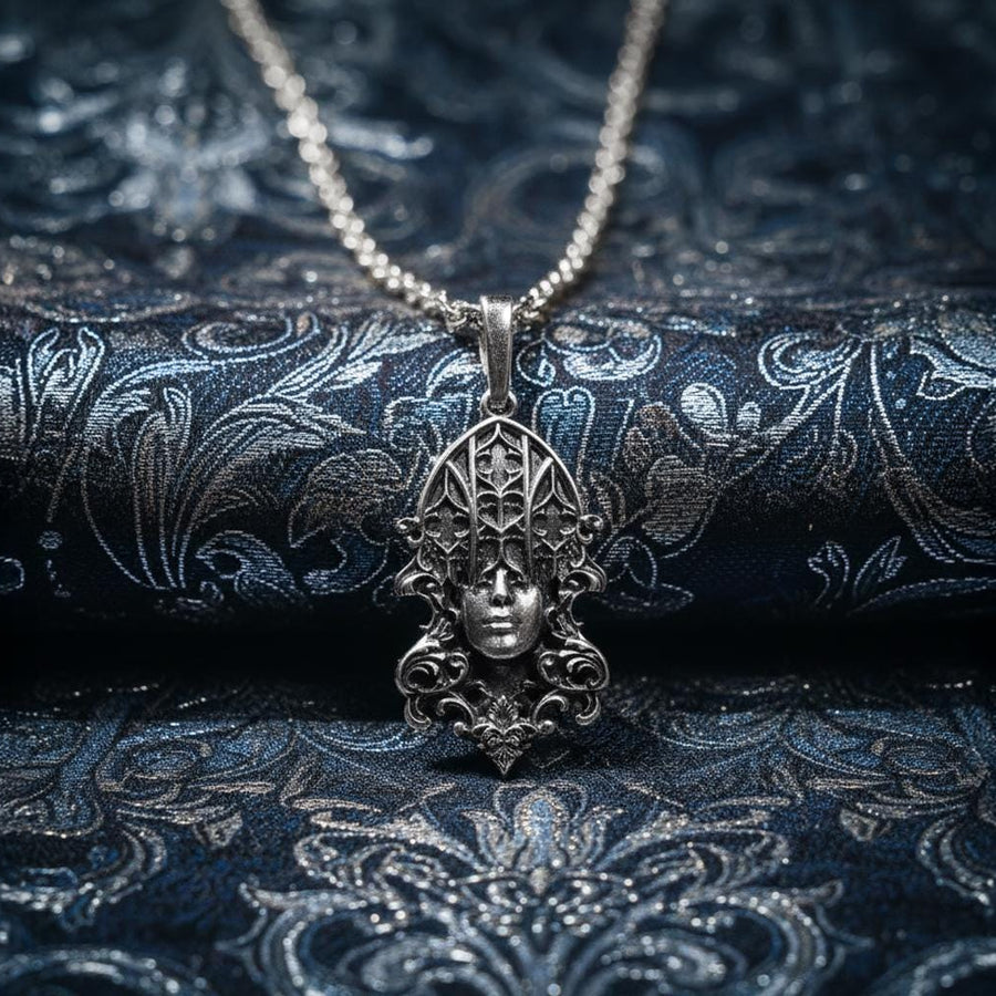 A detailed studio shot of a sterling silver pendant resting on a dark, textured stone surface. The design features a realistic human face in the center, but the forehead and eyes are obscured by a grid of Gothic window tracery (vertical bars and trefoils). The chin is framed by swirling Art Nouveau-style acanthus leaves. The silver is heavily oxidized, giving the face the appearance of a weathered stone statue. (etsy image id: 7448678222)