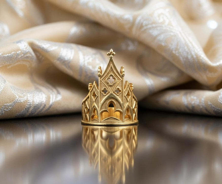 A clean studio shot of a sculptural sterling silver ring resting on a matte grey surface. The ring depicts a Gothic building facade with a tall, triangular central peak (gable) filled with geometric cross-shaped tracery. Flanking the center are lower pointed arches and vertical buttresses that wrap around the band. The silver is matte-finished with dark oxidation in the recesses to mimic stone shadows. (etsy image id: 7452370200)