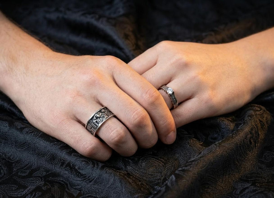 A cinematic studio shot of a matching two-piece ring set. The bottom ring is a wide silver band featuring a detailed relief carving of the couple from Gustav Klimt's "The Kiss." The top ring is a narrower engagement band that mimics the geometric patterns of the painting and holds a round, amber-colored gemstone. The background is a warm, golden haze, reflecting the "Golden Phase" of the original artwork.