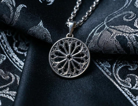 A high-contrast studio shot of a circular sterling silver pendant hanging from a chain. The design features a "Rose Window" motif—a central four-leaf clover (quatrefoil) surrounded by radiating spokes and intricate arches. The raised tracery is polished silver, while the negative space is chemically oxidized to a matte black, mimicking the depth of a stone window frame. (etsy image id: 7493952667)