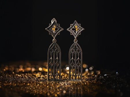 A clear studio shot of a pair of long sterling silver earrings resting on a matte grey surface. The earrings are articulated in two parts. The top is a diamond-shaped stud containing a four-lobed "quatrefoil" motif. The bottom is a long, rectangular drop with an arched top, filled with vertical "lancet" tracery lines. The background metal is dark (oxidized), making the raised silver lines pop. (etsy image id: 7496908697)