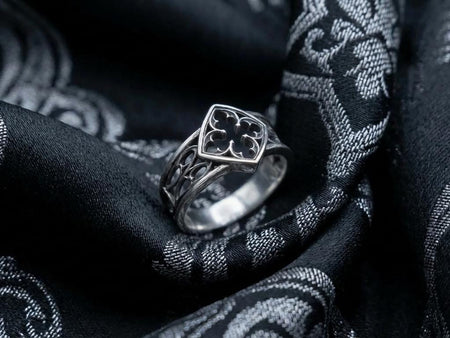 A close-up of a handcrafted sterling silver ring featuring a repeating pattern of Gothic pointed arches. The raised metal lines are highly polished, gleaming against a textured, matte black background created through heavy oxidation. The intricate relief mimics the stone tracery found in medieval cathedral windows, offering a rugged yet sophisticated appearance. The ring sits on a reflective black surface, highlighting the depth of the carving an (etsy image id: 7498411971)