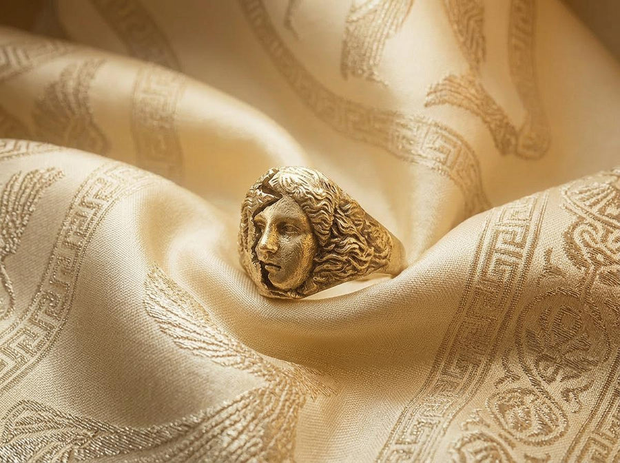 A high-contrast macro photograph of a heavy sterling silver ring resting against a pitch-black background. The ring features a three-dimensional sculpture of a classical Greek goddess's face, likely Athena. A jagged, deep crack splits the face vertically. The right side shows smooth, classical features, while the left side transitions into a rough, eroded, and porous texture resembling crumbling ancient stone. The silver is heavily oxidized t (etsy image id: 7831406732)