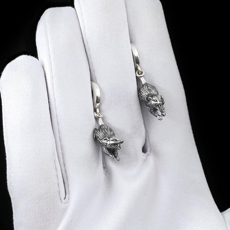 A close-up studio shot of sterling silver dangle earrings featuring detailed opossums. The animals are depicted with open mouths and textured fur, hanging from polished lever-back clasps. The metal is heavily oxidized in the recesses to enhance the realistic, rugged appearance of the marsupials against a white fabric background.