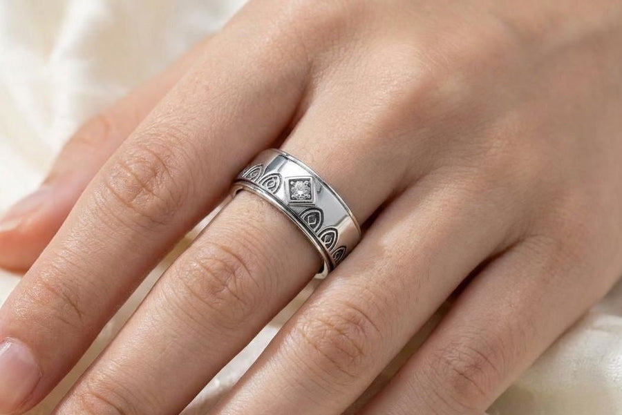 A high-resolution macro photograph of a matching sterling silver gothic wedding ring set resting on softly draped, luxurious white satin. The set features a wider masculine band and a slightly narrower feminine band. Both rings display a continuous engraved arcade of pointed medieval arches along the bottom edge, centering on a polished geometric rhombus frame that holds a brilliant round white gemstone. The polished silver beautifully contrasts  (etsy image id: 7928017042)