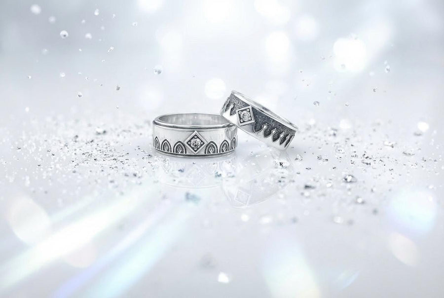 A high-resolution macro photograph of a matching sterling silver gothic wedding ring set resting on softly draped, luxurious white satin. The set features a wider masculine band and a slightly narrower feminine band. Both rings display a continuous engraved arcade of pointed medieval arches along the bottom edge, centering on a polished geometric rhombus frame that holds a brilliant round white gemstone. The polished silver beautifully contrasts  (etsy image id: 7928017042)