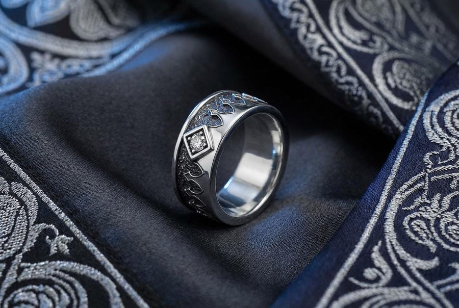 A high-resolution macro photograph of a matching sterling silver gothic wedding ring set resting on softly draped, luxurious white satin. The set features a wider masculine band and a slightly narrower feminine band. Both rings display a continuous engraved arcade of pointed medieval arches along the bottom edge, centering on a polished geometric rhombus frame that holds a brilliant round white gemstone. The polished silver beautifully contrasts  (etsy image id: 7928017042)