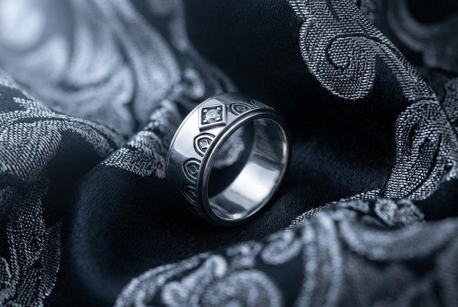 A high-resolution macro photograph of a matching sterling silver gothic wedding ring set resting on softly draped, luxurious white satin. The set features a wider masculine band and a slightly narrower feminine band. Both rings display a continuous engraved arcade of pointed medieval arches along the bottom edge, centering on a polished geometric rhombus frame that holds a brilliant round white gemstone. The polished silver beautifully contrasts  (etsy image id: 7928017042)