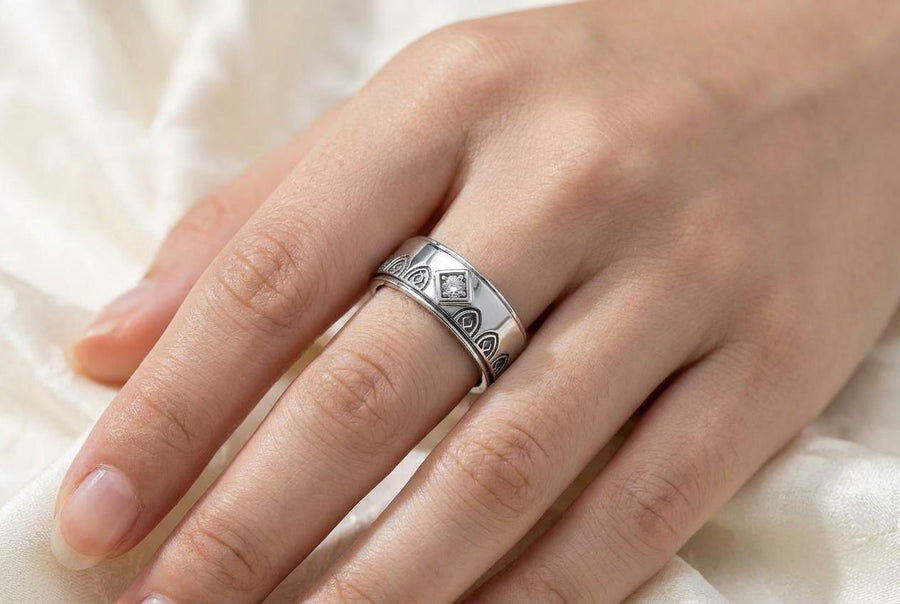 A high-resolution macro photograph of a matching sterling silver gothic wedding ring set resting on softly draped, luxurious white satin. The set features a wider masculine band and a slightly narrower feminine band. Both rings display a continuous engraved arcade of pointed medieval arches along the bottom edge, centering on a polished geometric rhombus frame that holds a brilliant round white gemstone. The polished silver beautifully contrasts  (etsy image id: 7928017042)