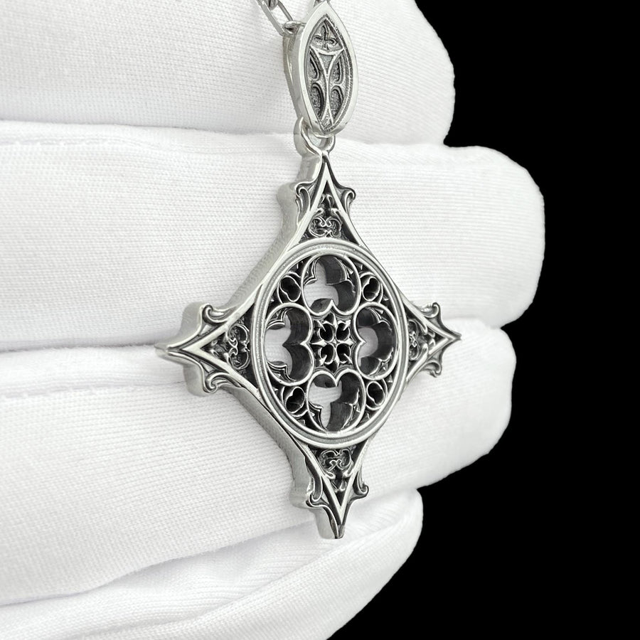 Showcasing exceptional openwork silversmithing, this gothic cross pendant demonstrates precise micro-casting techniques. The slender mullions and tracery lines are perfectly symmetrical and structurally sound, maintaining the airy lightness of a true cathedral window. A sturdy, intricately decorated silver bail is seamlessly integrated into the top point, ensuring the heavy charm hangs perfectly balanced on its chain. (etsy image id: 8027043505)
