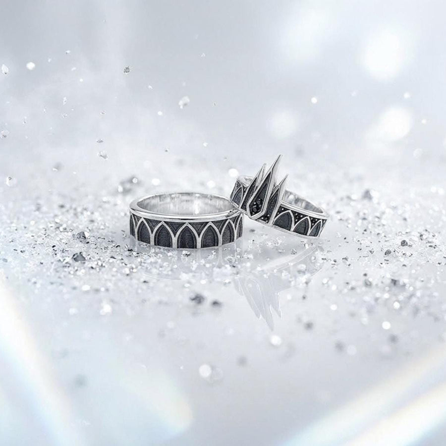 A high-resolution studio photograph of a matching sterling silver gothic wedding ring set resting on a reflective black background. The set features a wide band with a continuous arcade of pointed lancet arches. The companion engagement ring beautifully matches the arch design, forming a dramatic tiara silhouette accented by small, round black gemstones set within the structural peaks. The silver is heavily oxidized.